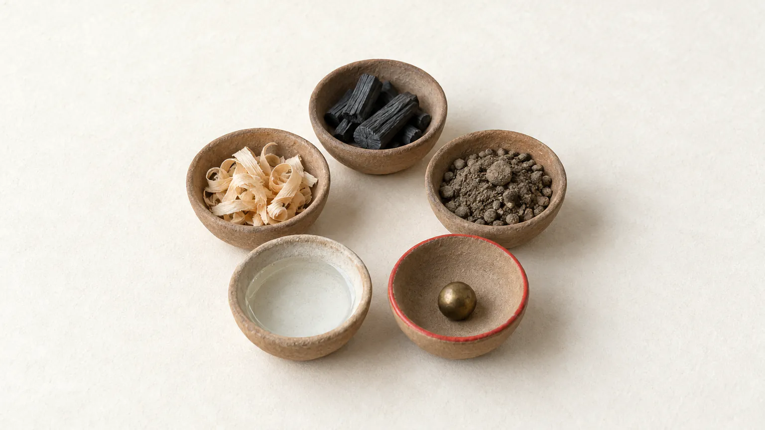 Five unglazed clay dishes in a gentle arc holding wood shavings, charcoal, earth, a bronze bead and clear water