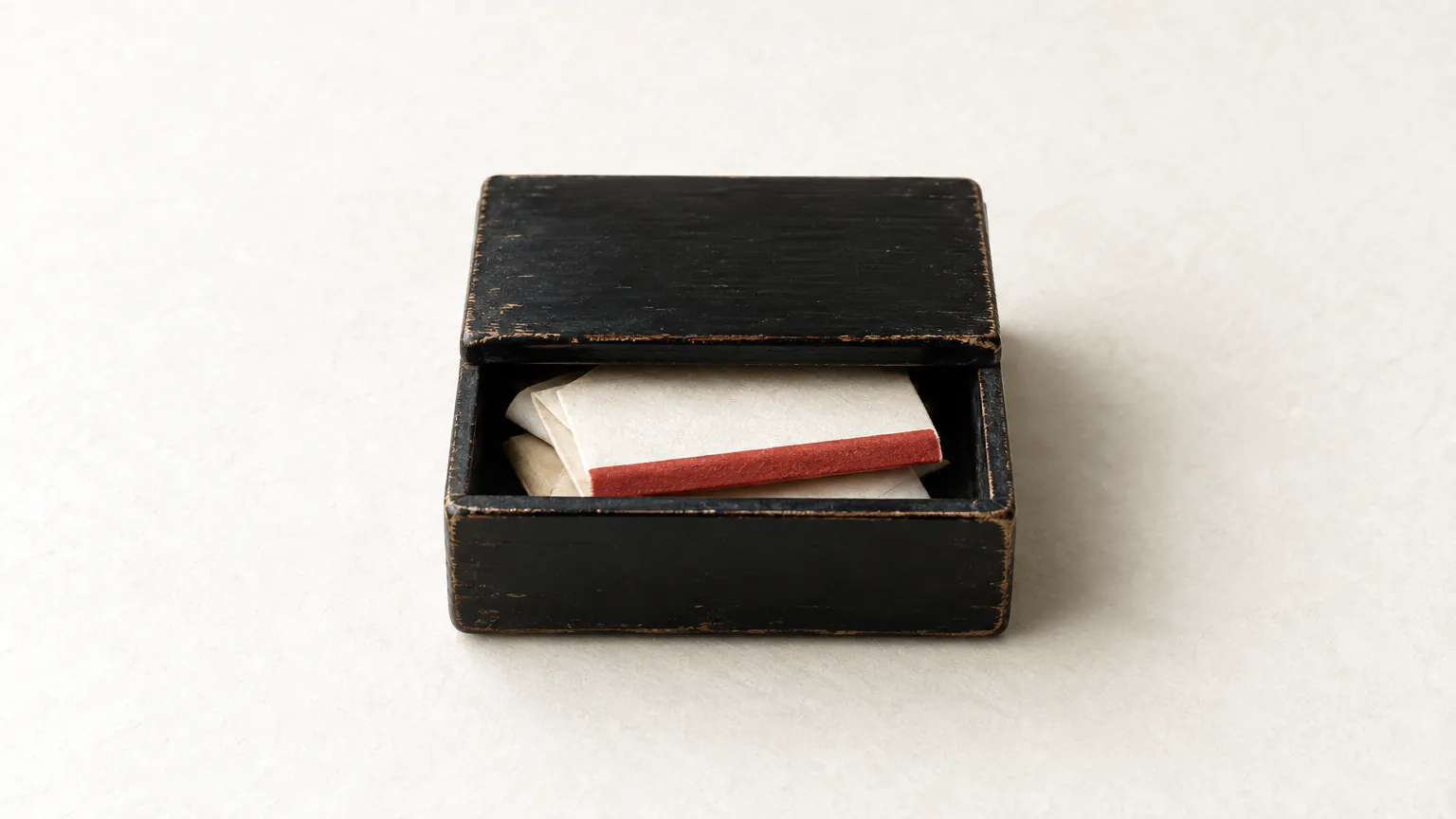 A black lacquer box with its lid ajar and folded blank slips inside