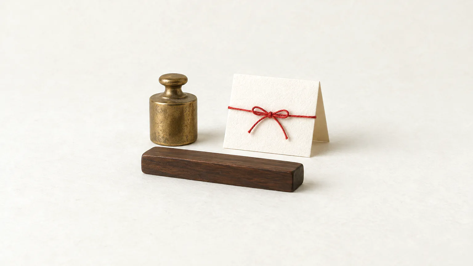 A small brass weight, a short dark wooden bar and a folded card tied with red thread on warm paper