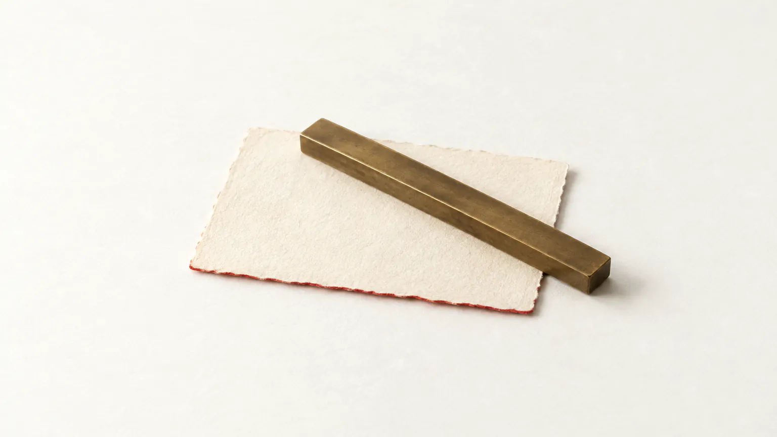 A plain bronze ruler without markings resting on a blank sheet of paper