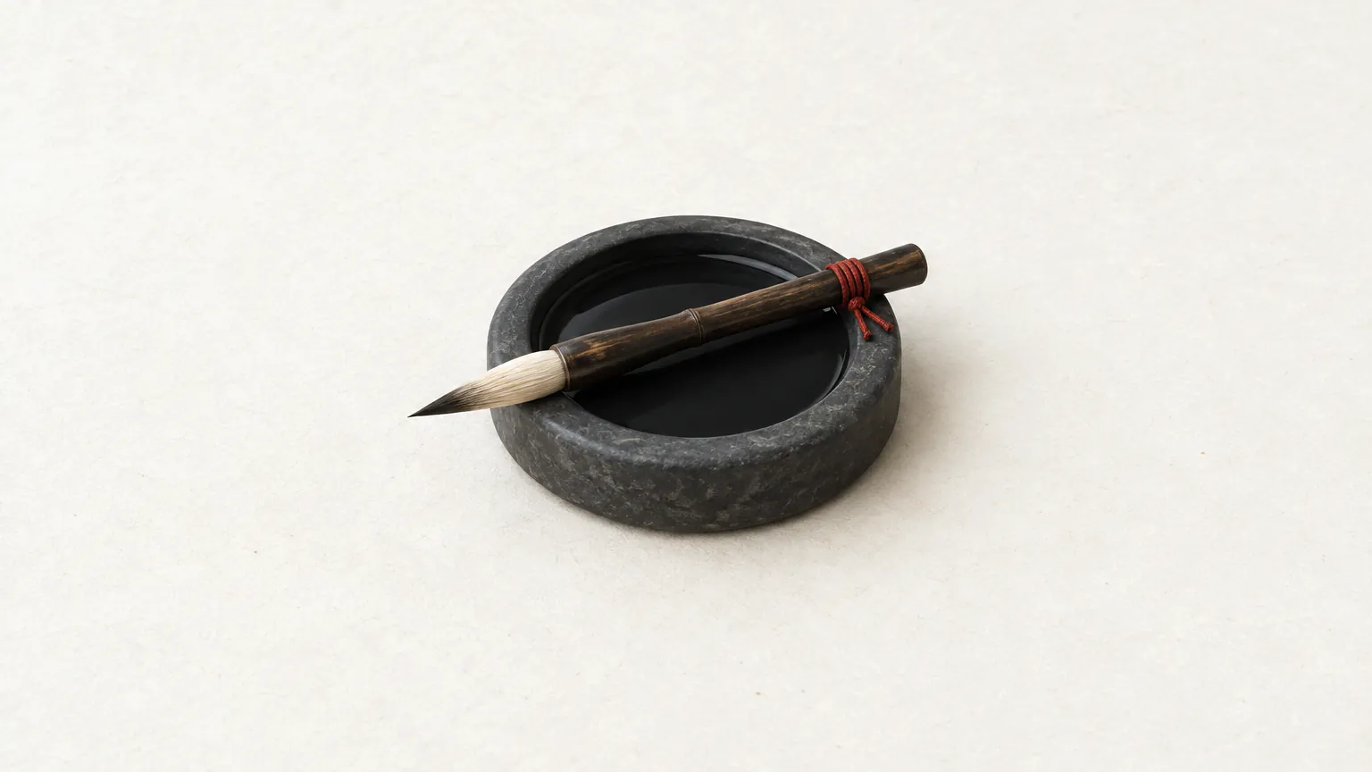 A round ink stone filled with black ink, a calligraphy brush resting across it, its handle tied with red thread
