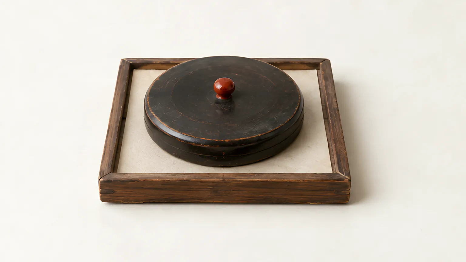 四角い木の盆に、朱色の小さなつまみが付いた黒漆の丸い蓋が載っている。四角い地盤に丸い天盤を重ねたような姿
