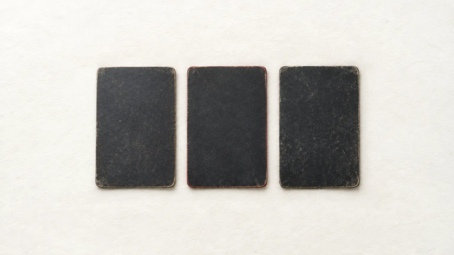 Three face-down cards with plain dark backs laid in a row, the middle one edged in red